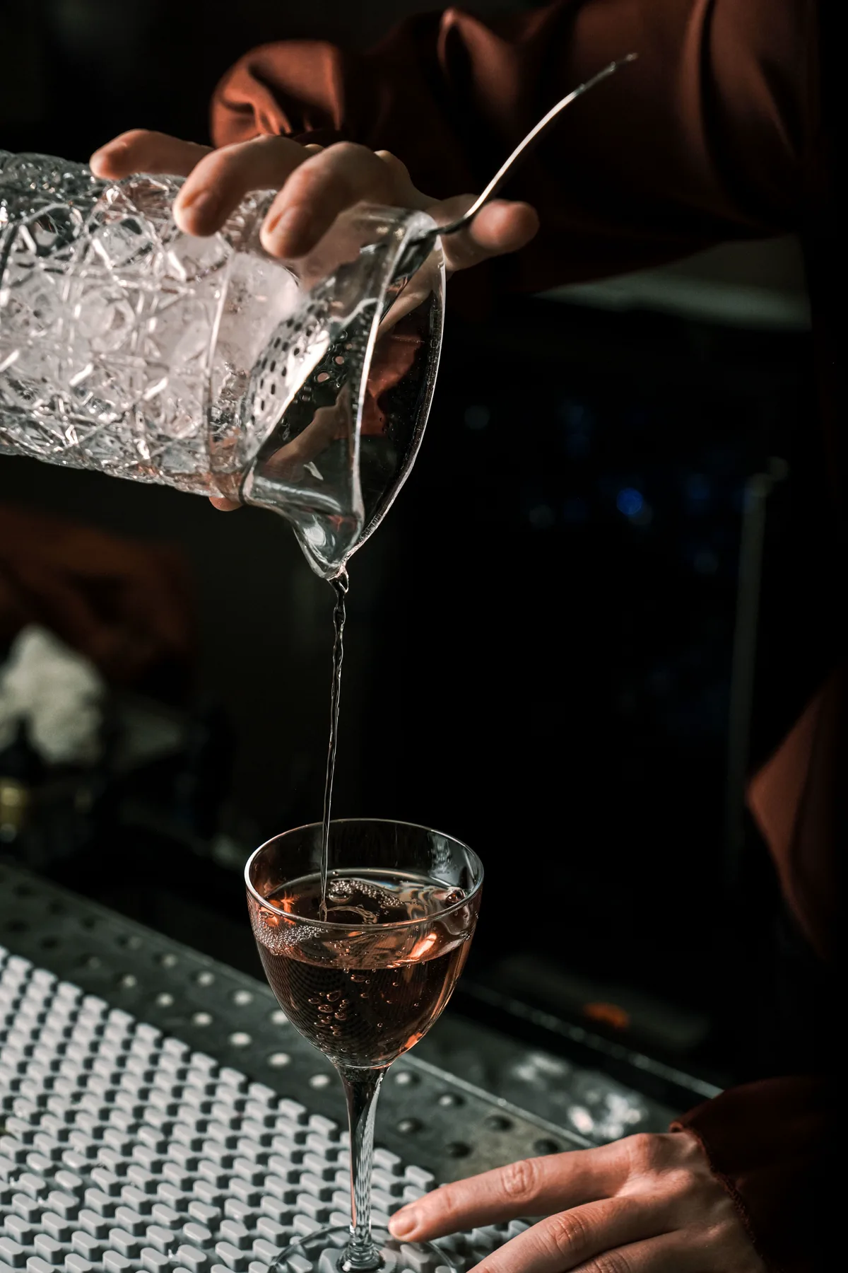Bartender pouring a clear cocktail in a dark bar